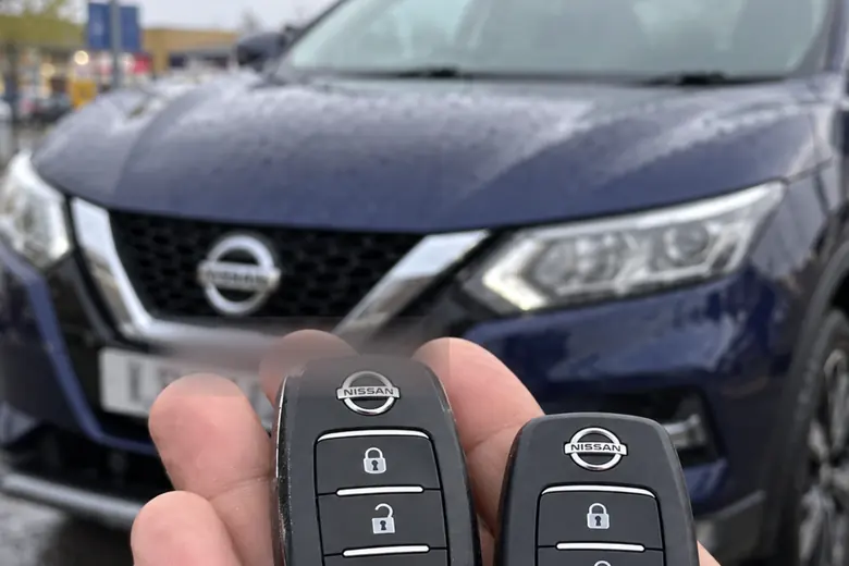 A car key held in front of a Nissan Qashqai